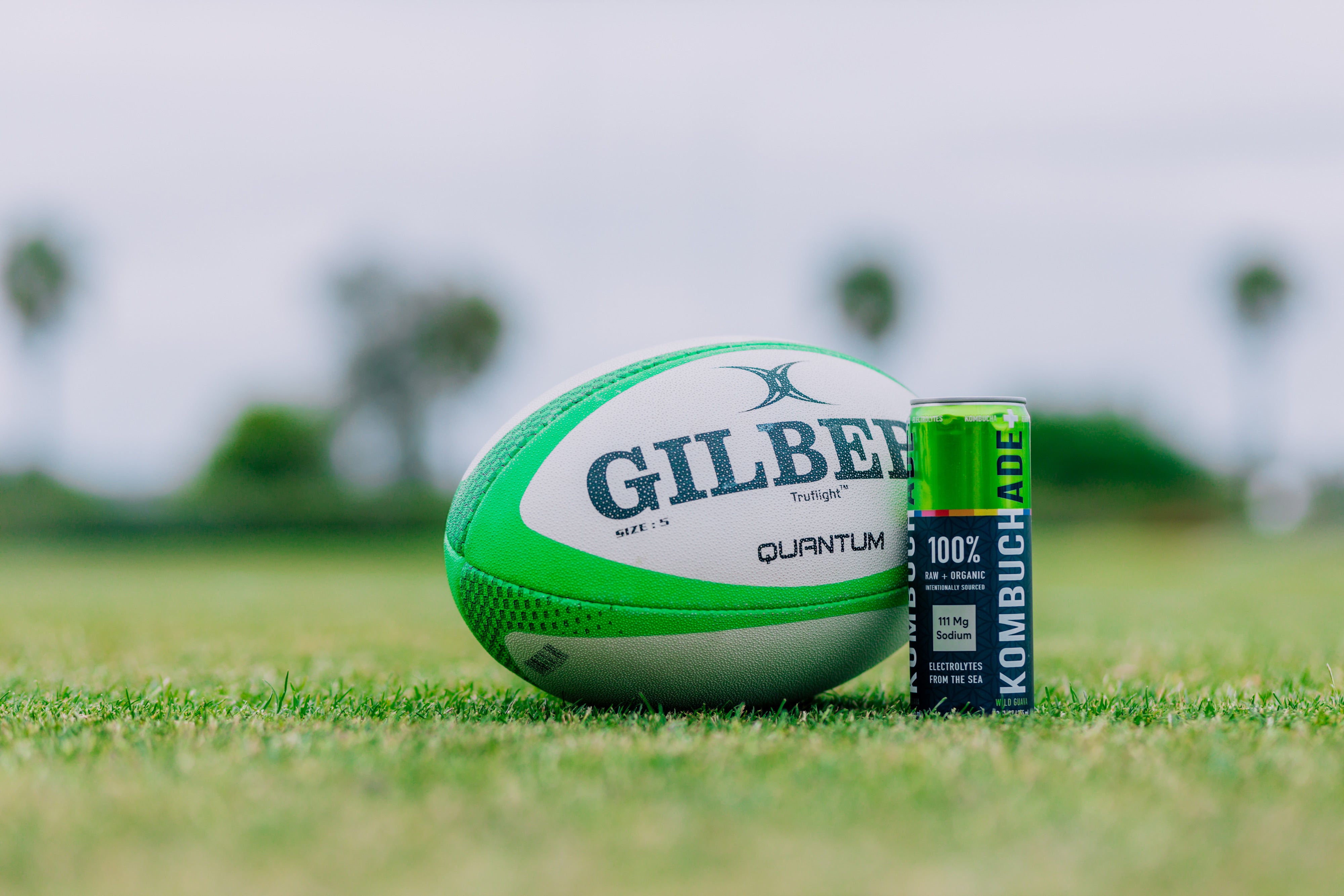 green rugby ball next to can of Wild Guava Kombuchade on green rugby field