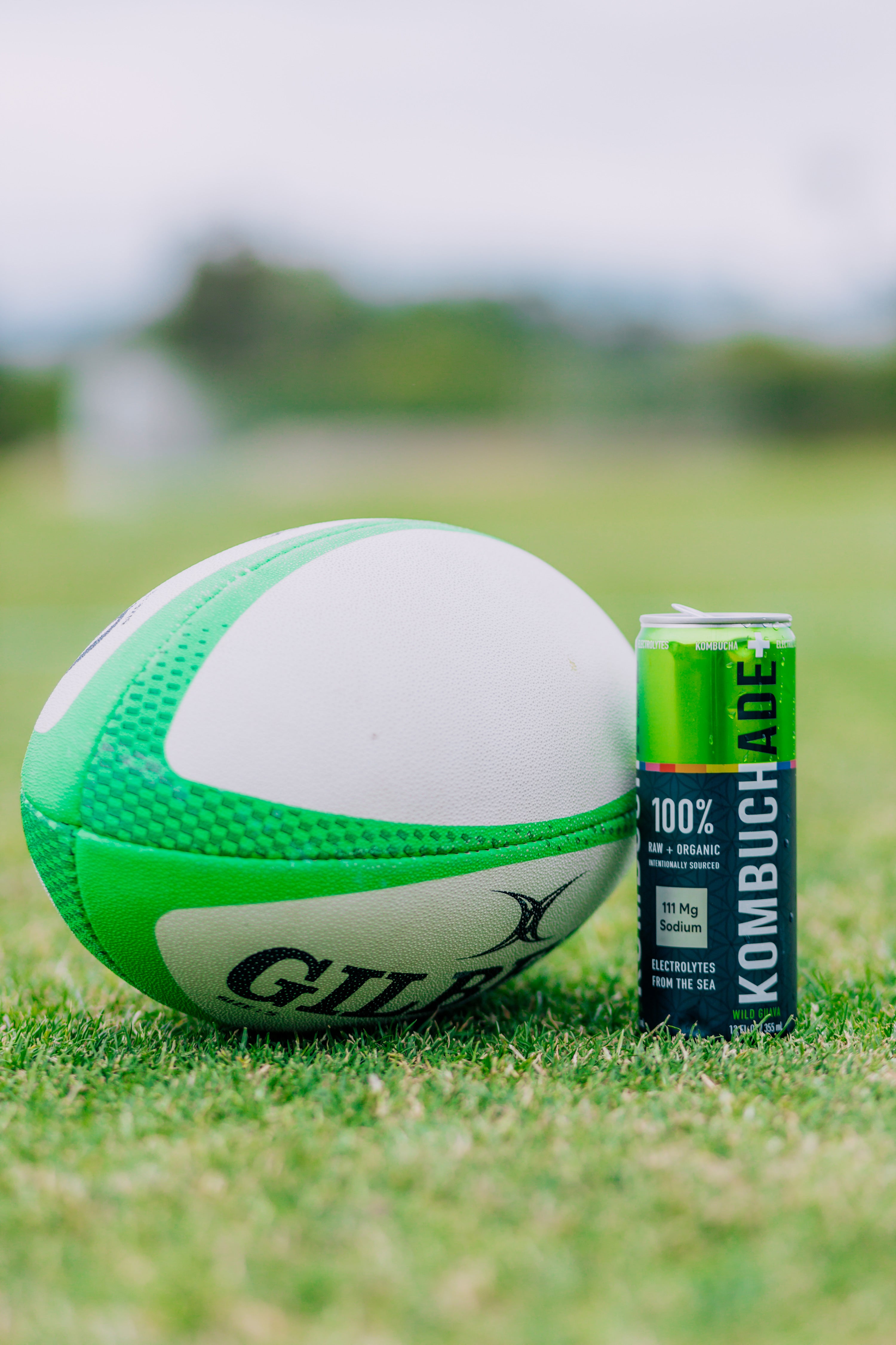 green rugby ball next to can of Wild Guava Kombuchade on green rugby field