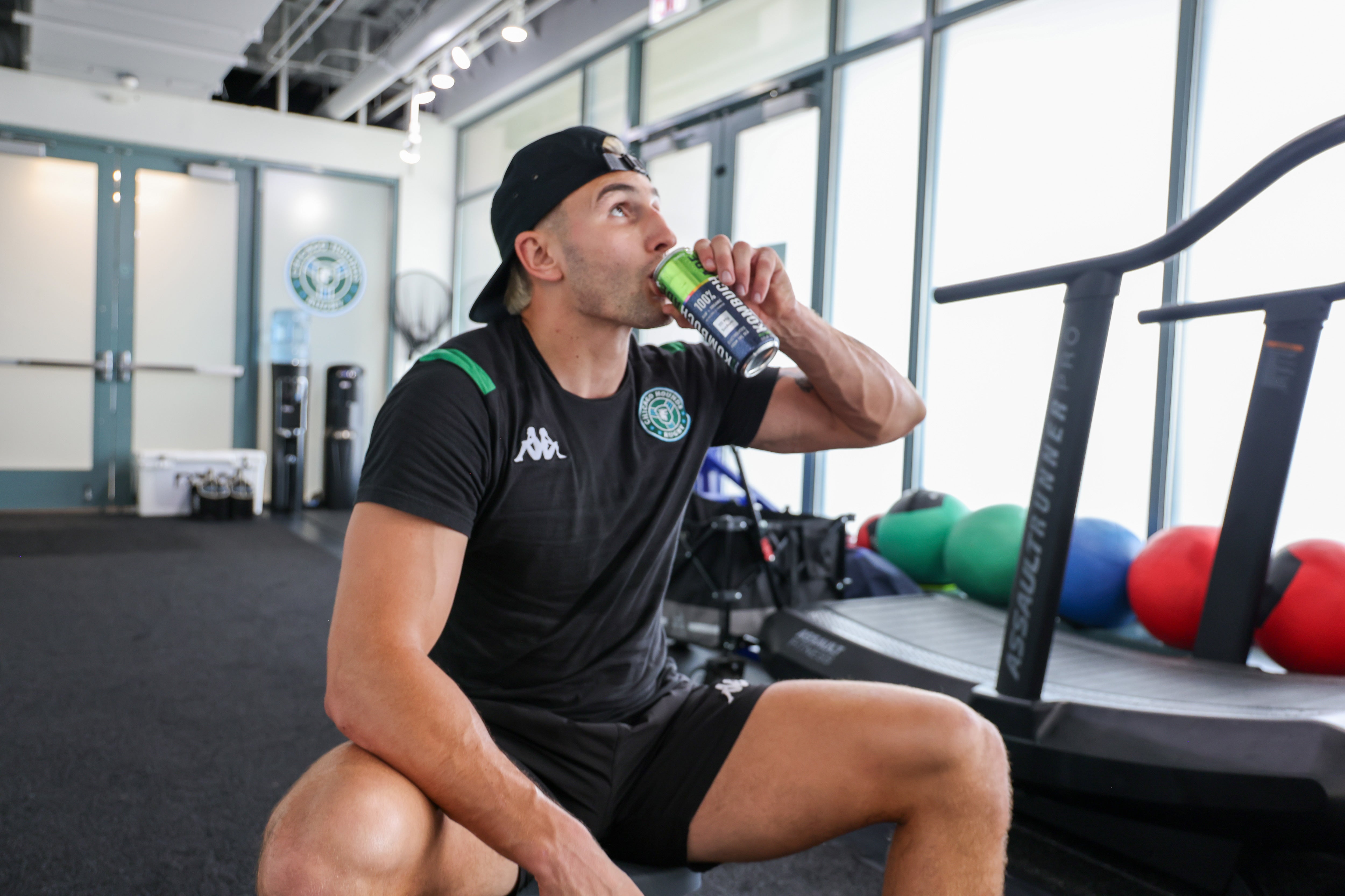 Athlete drinking a can of Wild Guava Kombuchade sitting on a bench in gym