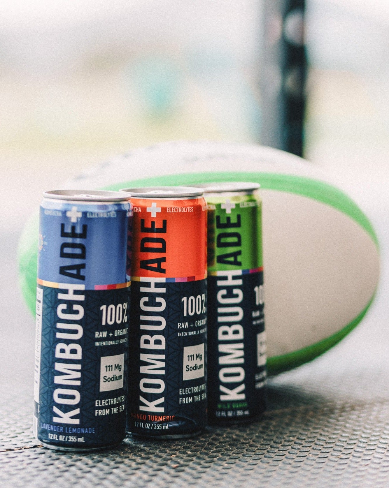 green rugby ball behind 3 cans of different flavors of Kombuchade