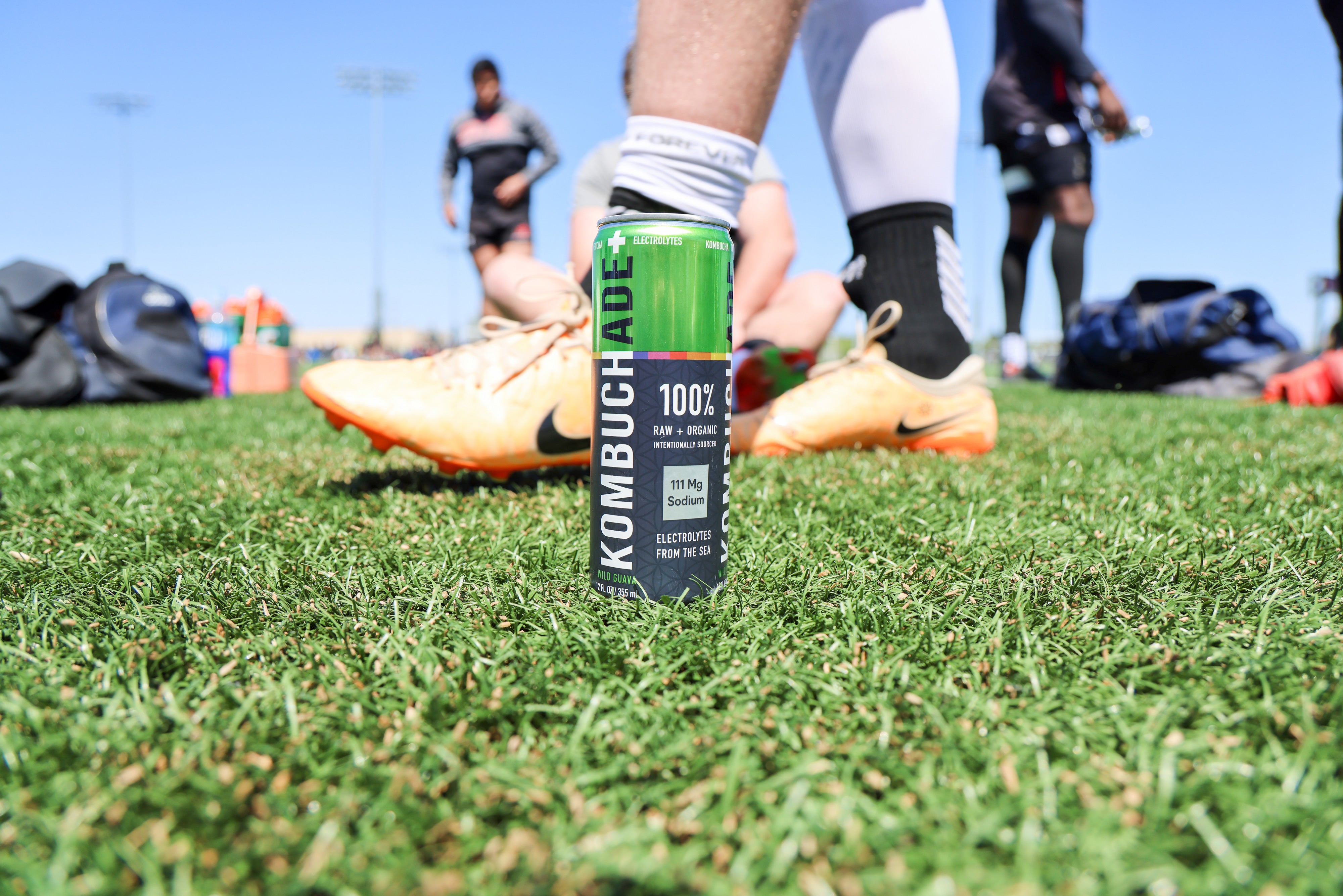 can of Wild Guava Kombuchade on rugby field while athlete walks by wearing yellow rugby shoes