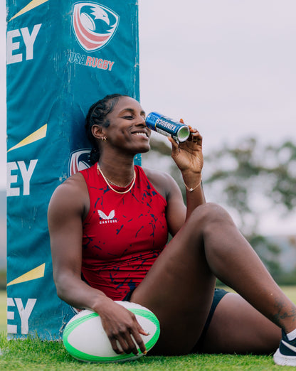 Naya Tapper USA rugby team athlete smiling while drinking lavender lemonade Kombuchade sitting on rugby field