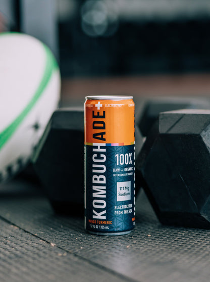 can of mango turmeric kombuchade sitting on floor with weights and rugby ball