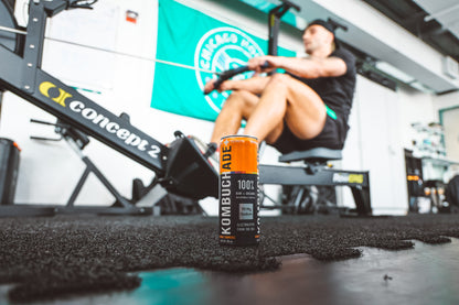 Athlete in gym on a rower with a can of mango turmeric Kombuchade