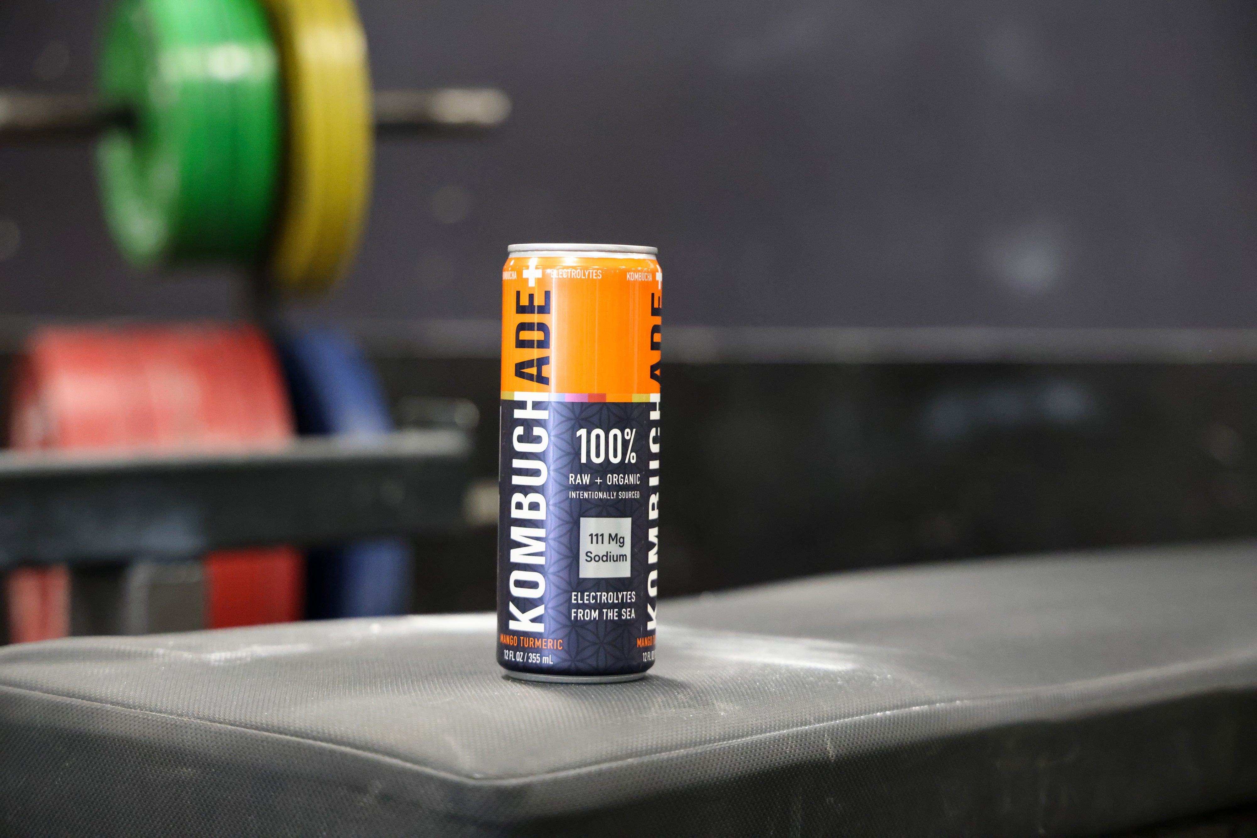 a can of Mango Turmeric Kombuchade sitting on a bench in a gym